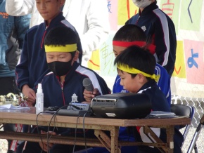 校庭の放送席でマイクを持ってアナウンスをする児童たちの写真