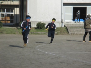 校庭でリレーのバトンを持って走る児童たちの写真
