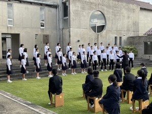 校庭で生徒たちが合唱を披露している写真