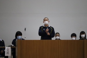 講堂で生徒がマイクを持って発表する写真