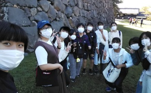 城跡の石垣前でマスク姿の生徒たちが記念撮影する写真