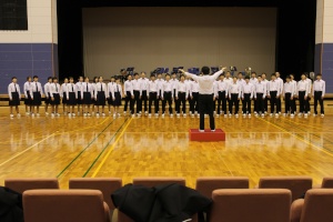 体育館の舞台で指揮者の前で合唱する生徒たちの写真