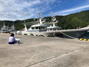 港で漁船を前にスケッチをする児童の写真