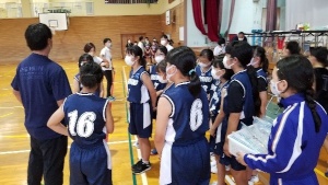 体育館で試合前に話を聞くバスケットボール部の児童たちの写真