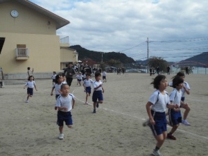 校庭を走る低学年の児童たちのマラソン大会の写真