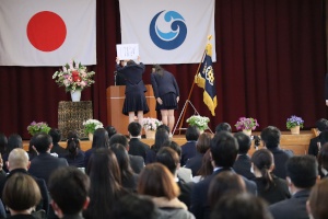 体育館で卒業証書授与式を行う生徒と観客の写真