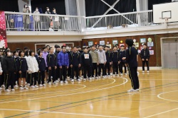 体育館で整列している生徒たちに向かって話をする先生の写真