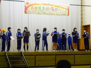 体育館の舞台で「6年生を送る会」の発表をしている児童たちの写真