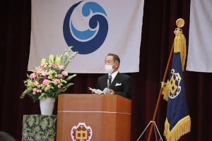 体育館のステージ上で校長先生が式辞を述べている様子の写真