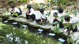 池に白い紙のようなものを浮かべて観察している生徒たちの写真