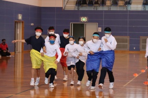 体育館で赤や緑のハチマキを付けた生徒たちが2人1組で団体競技を行っている写真