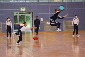 体操着を着た生徒たちがフリスビーのような円盤を取り合っている様子の写真