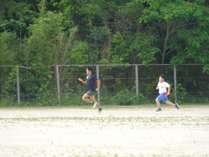 校庭を走るランナーの男性と、それを追うように併走する児童とのリレーの様子の写真