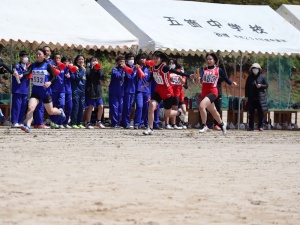 赤いメガホンで応援している生徒たちの目の前を走る選手の写真