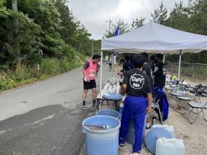 道路に面したテントを張った休憩所で水を用意している生徒たちの写真