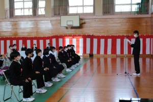 入学式で新入生が椅子に座り、代表者が前で挨拶をしている写真