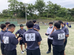 グラウンドで男子生徒とコーチが円を組んで作戦会議をしている写真