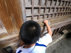 神社の建物の木の枠を雑巾で拭いている男子児童の写真