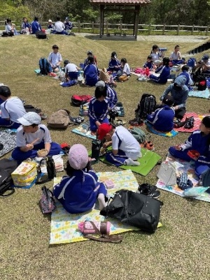芝生の上にレジャーシートを敷いてお弁当を食べる児童たちの写真