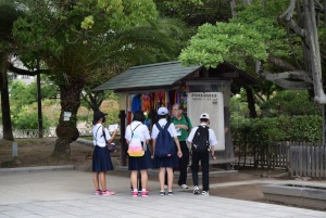 木々に囲まれた舗装された道に立つ4人の児童と1人の大人の写真