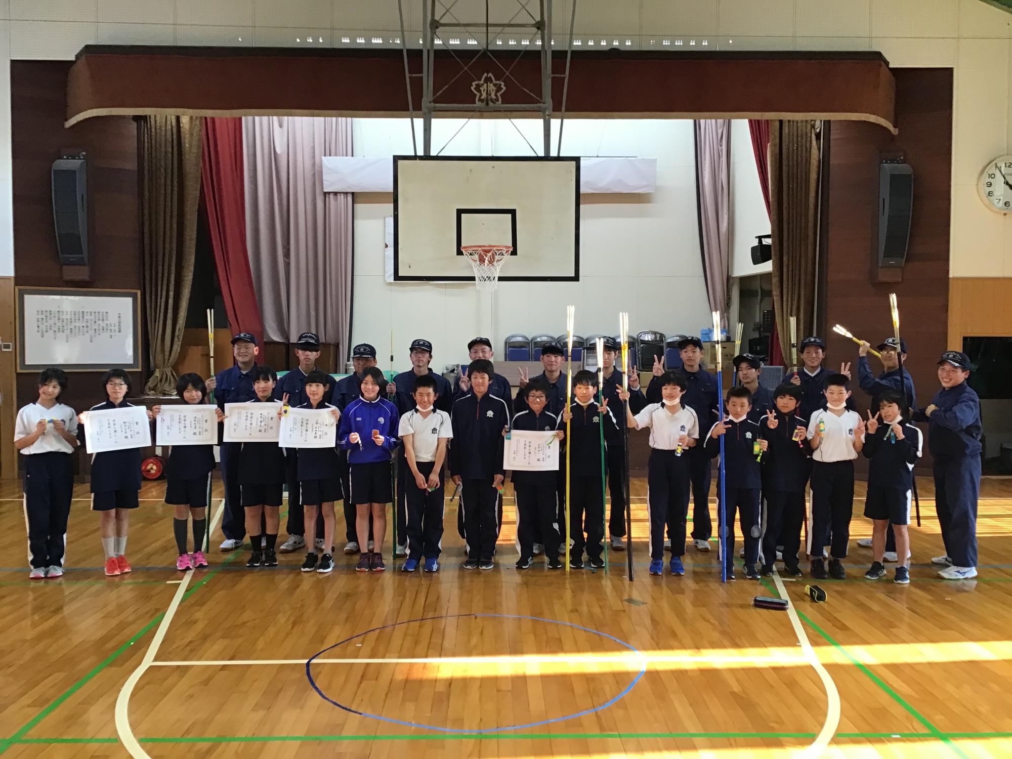 体育館で高校生と小学生たちが記念撮影をしている写真