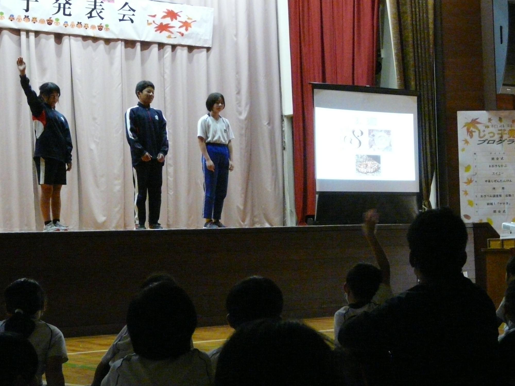舞台上でモニターを使って発表している児童たちの写真