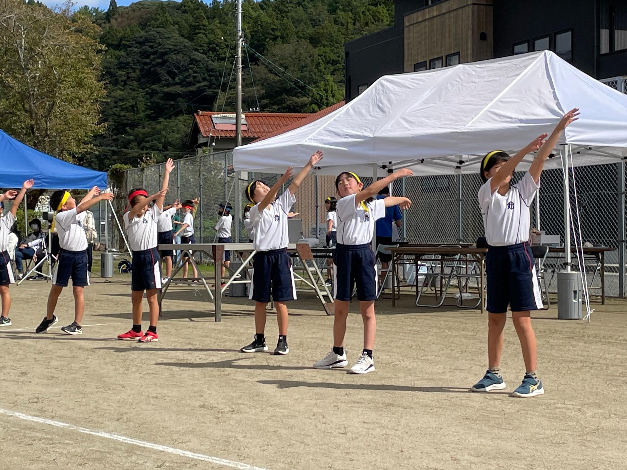 グラウンドで体操をして準備運動をする児童たちの写真