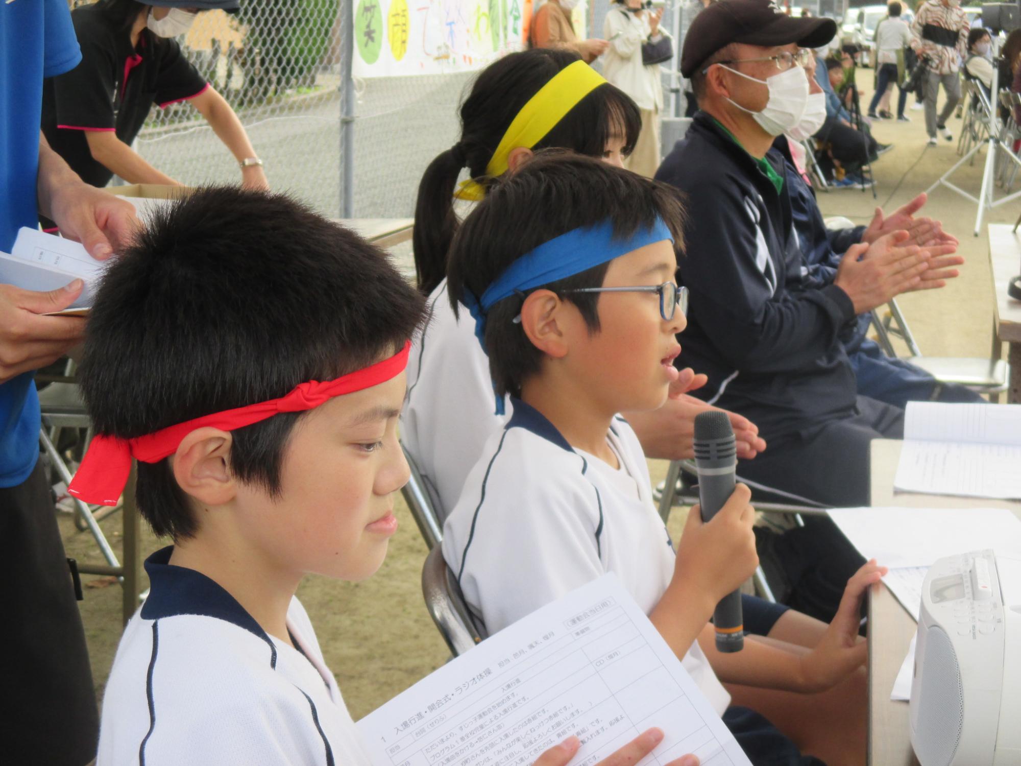 運動会でマイクを持ち実況を担当する児童たちの写真