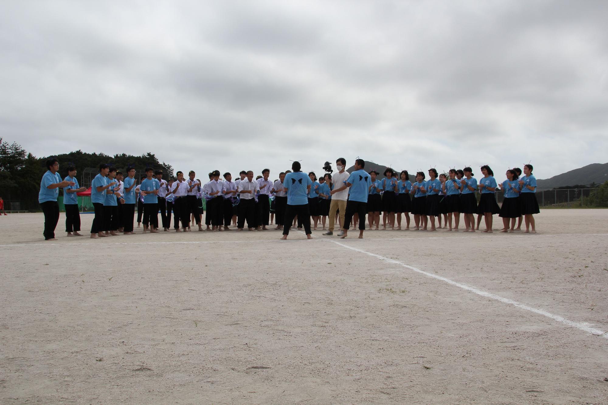 校庭で青いTシャツを着た生徒たちと制服を着ている生徒たちが集合している写真