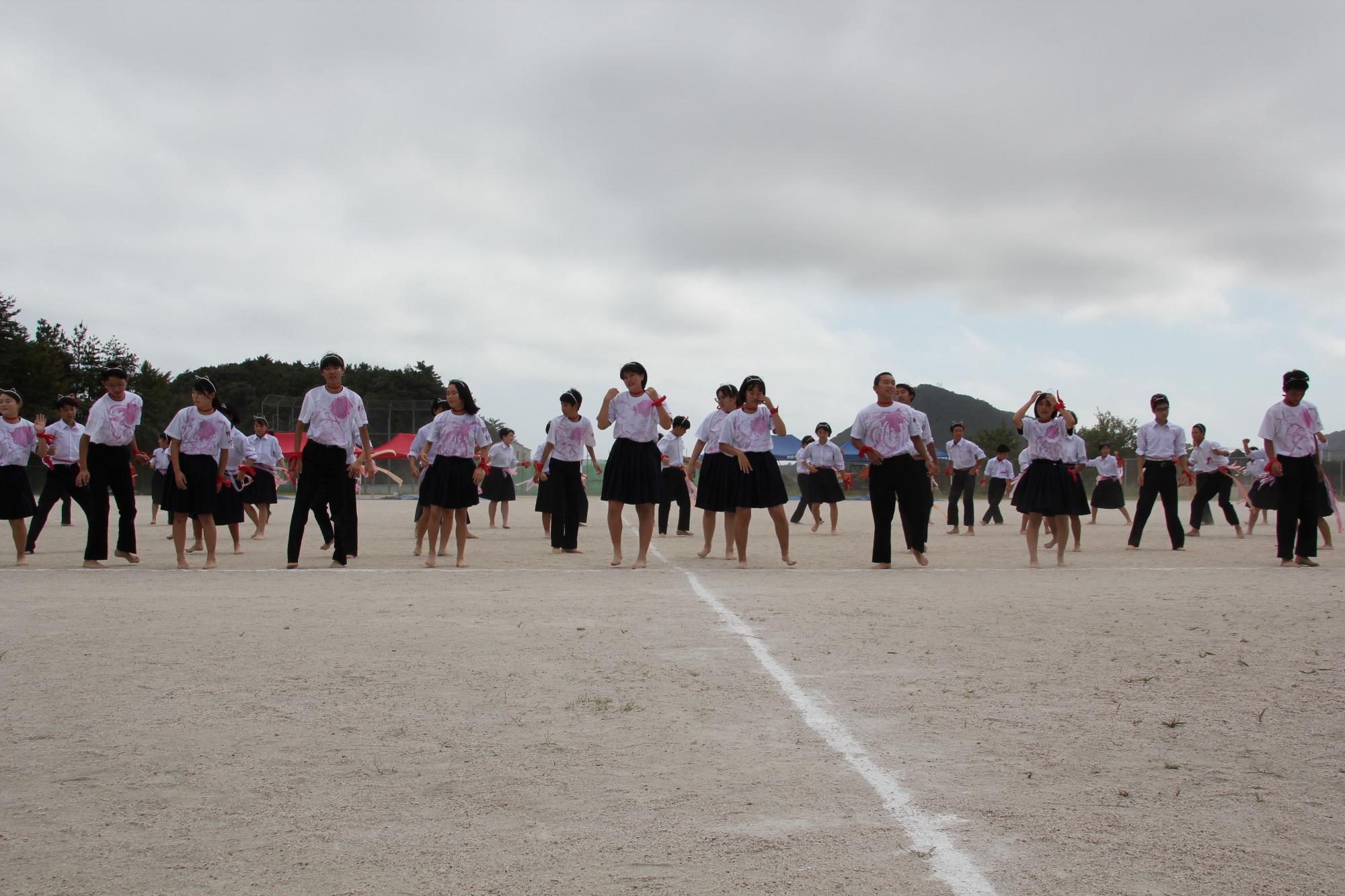 ピンクの模様が描かれている白いTシャツを着た生徒たちが整列している写真