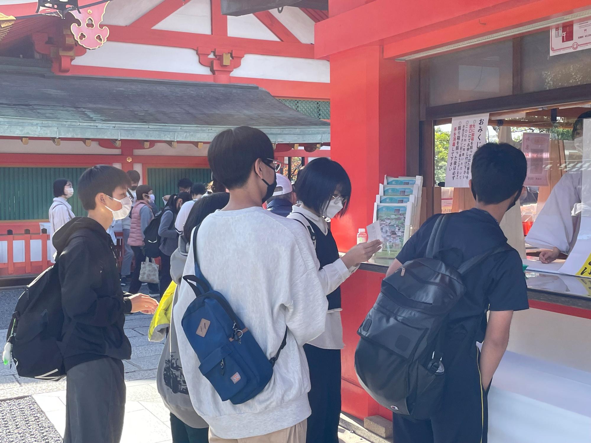 赤い建物でおみくじを買う生徒たちの写真