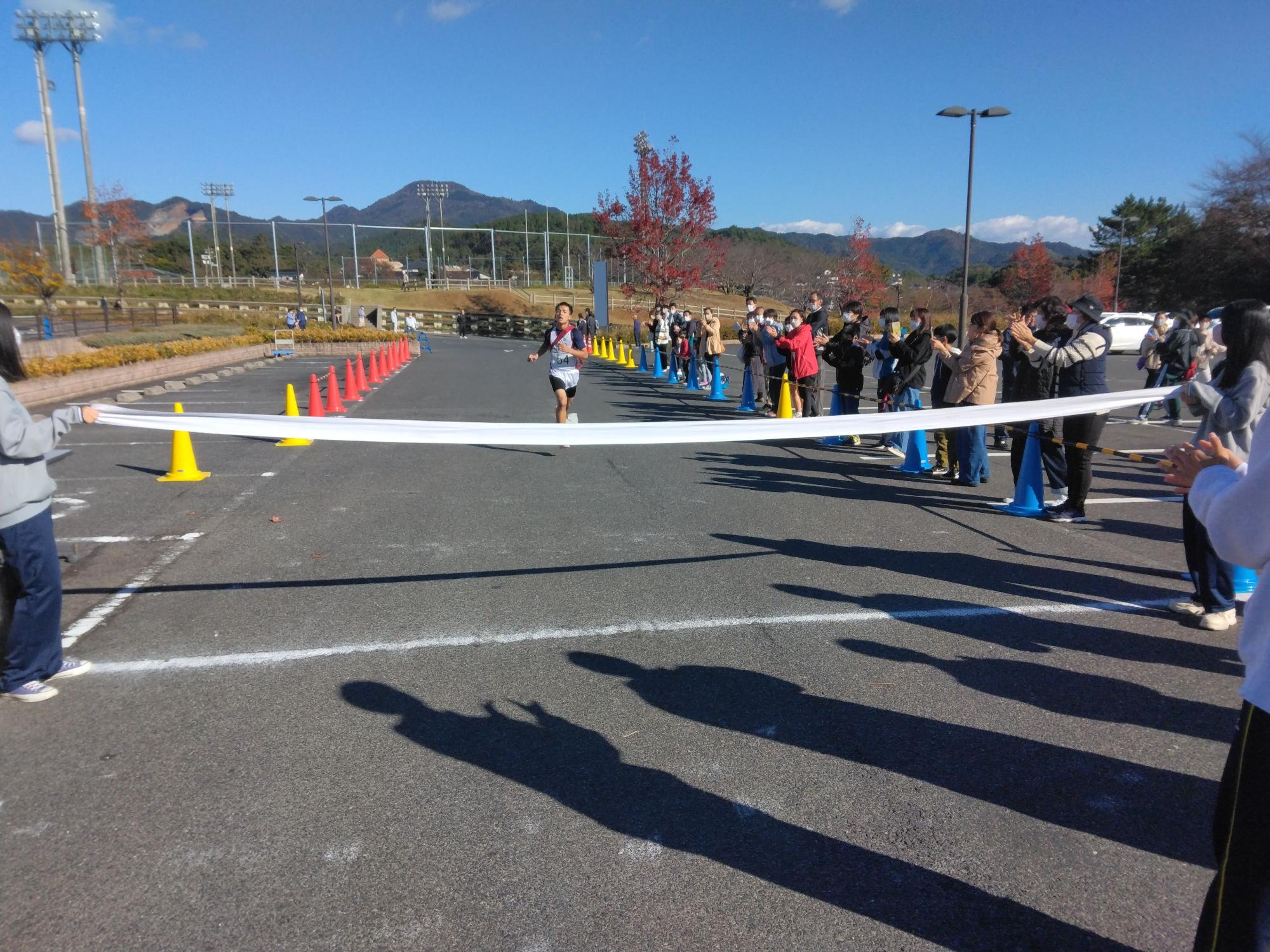 三角コーンが置かれた道路にてゴールテープに向かって走る生徒の写真