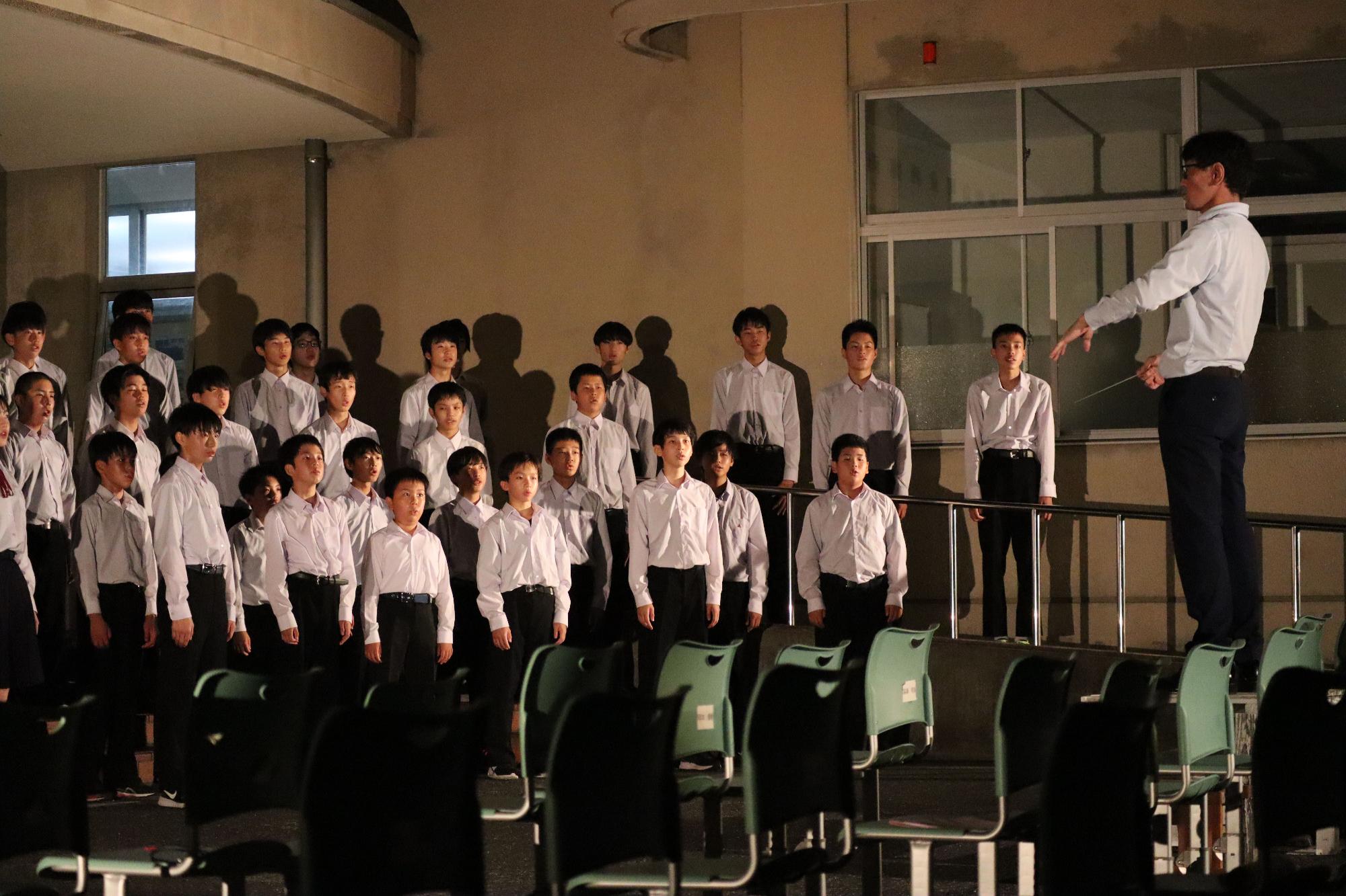 薄暗い部屋で指揮者に合わせて合唱する生徒たちの写真