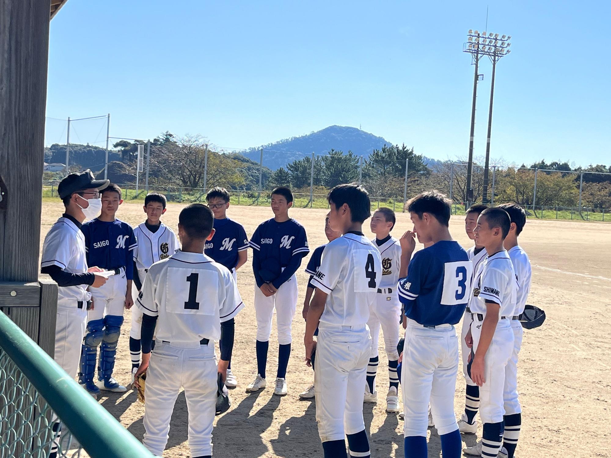 グラウンドで円になって話す野球のユニフォームを着た生徒たちの写真