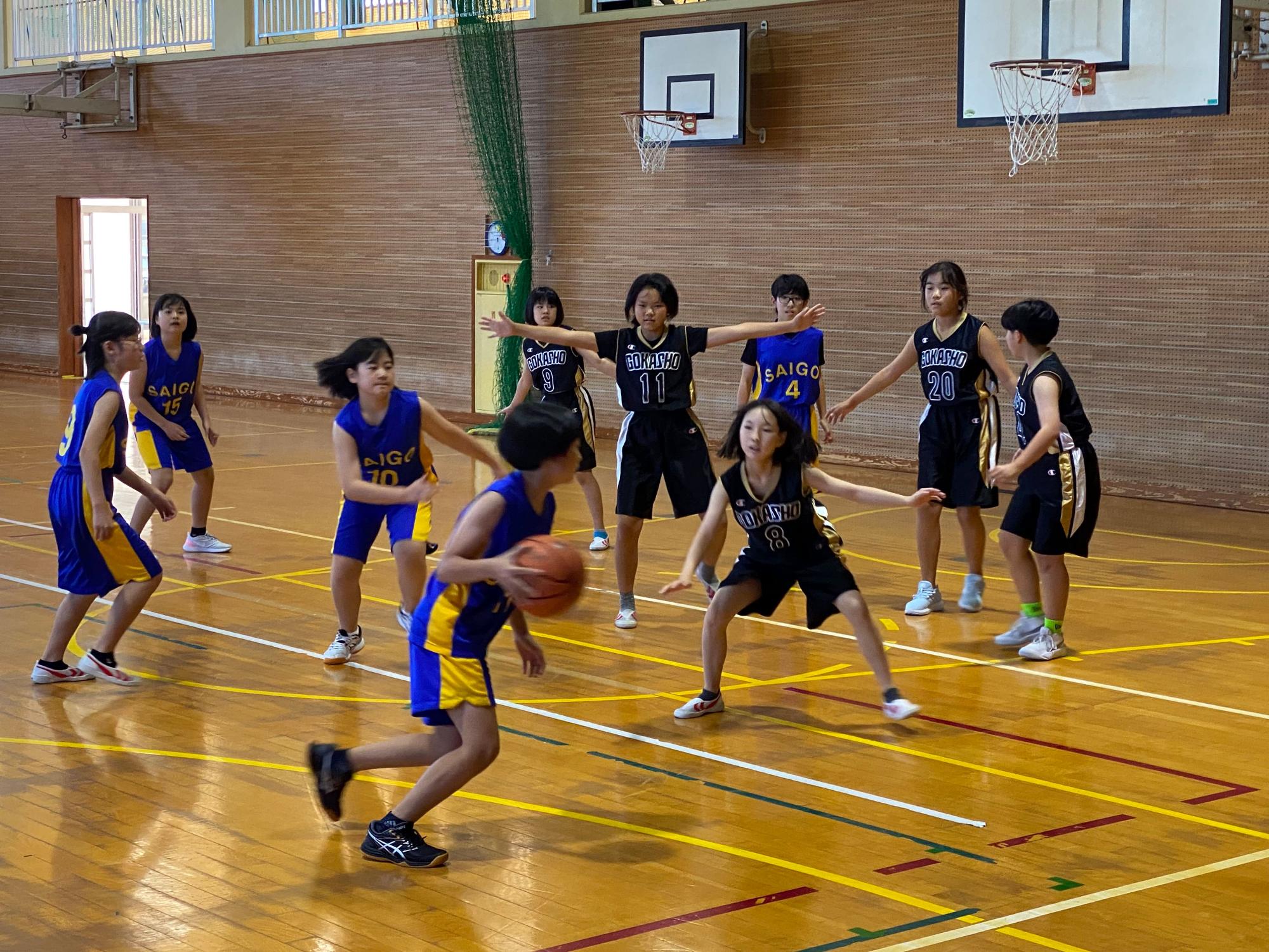 体育館のコートで女子児童たちがバスケットボールの試合をしている写真