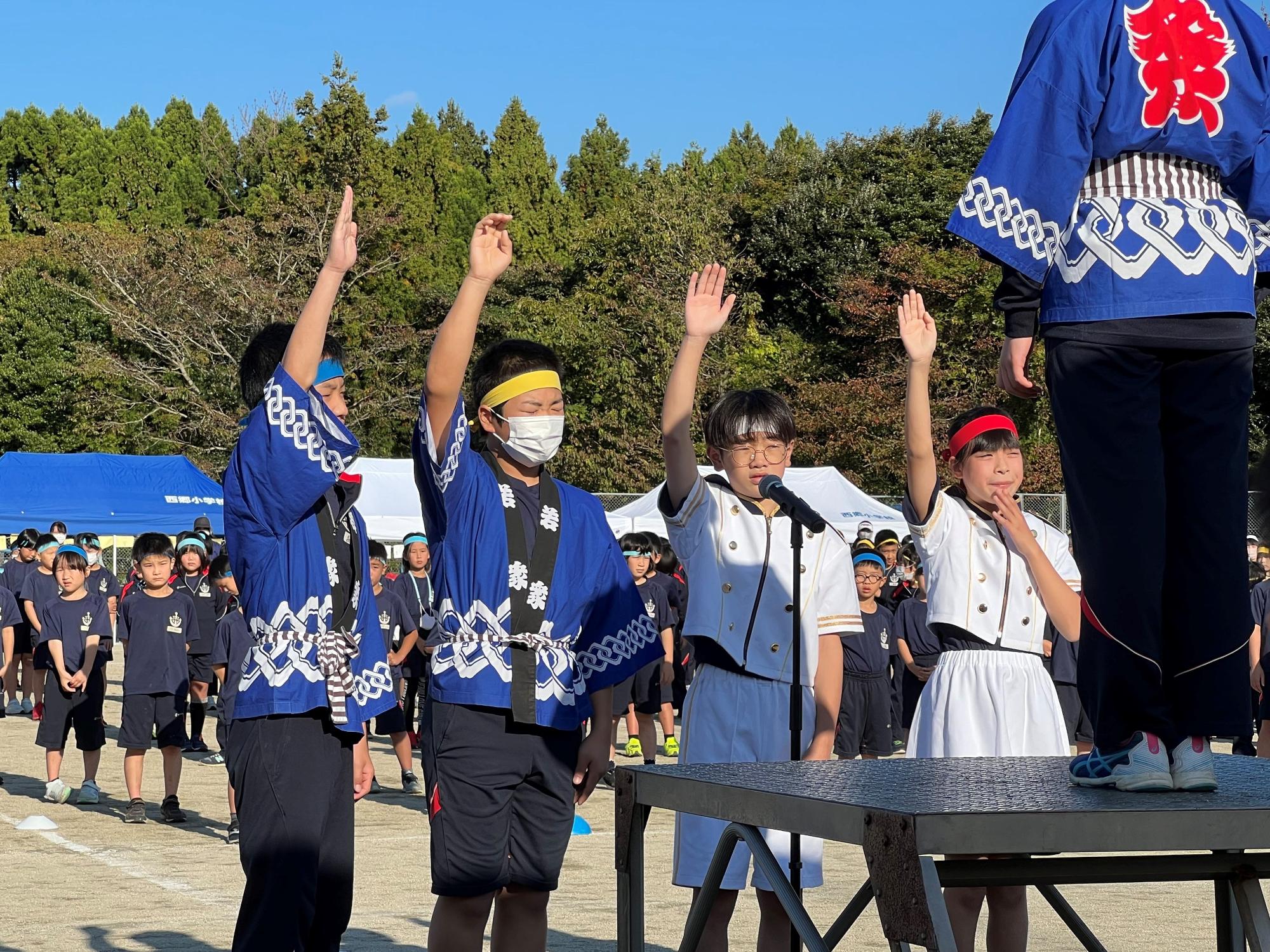校庭の壇上で代表の児童たちが手を挙げて選手宣誓をしている写真
