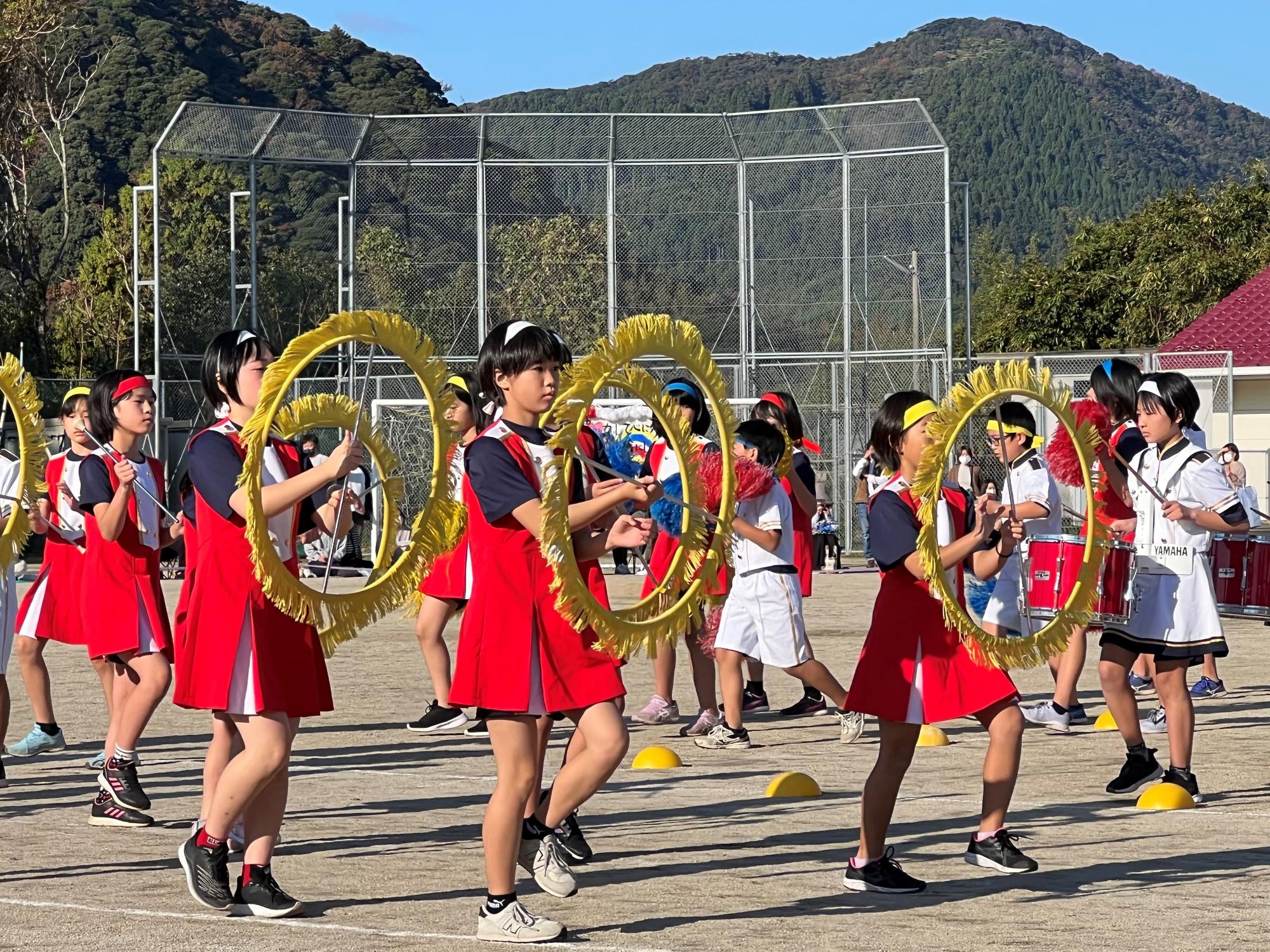 校庭で児童たちが輪っかを持ってマーチング演奏をしている写真