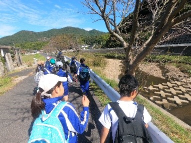 川沿いの道を児童たちが列になって歩いている写真