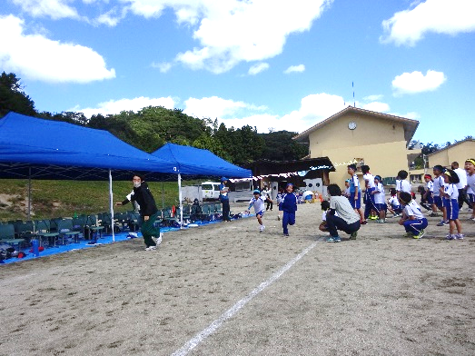 校庭のテントのそばで児童たちがリレーに参加して走っている写真