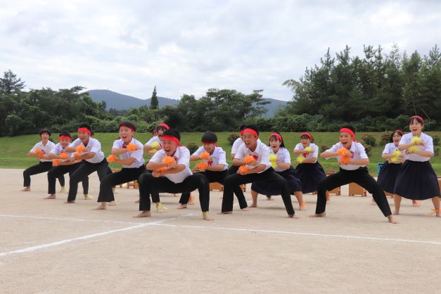 運動場で生徒たちが赤いハチマキをつけて踊っている写真