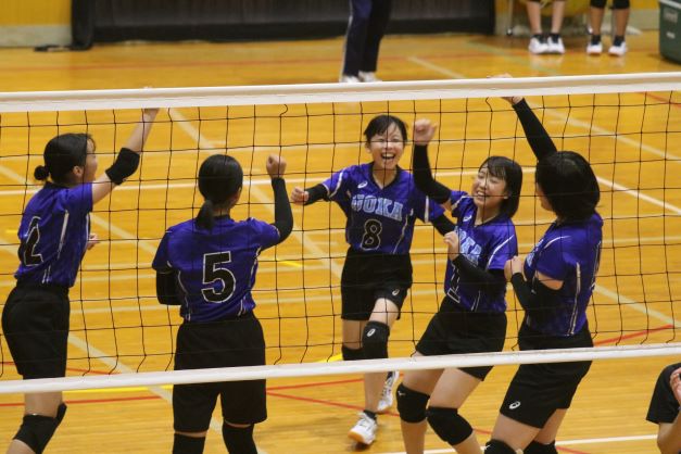 体育館で女子バレーボール部の生徒たちが試合中に喜んでいる写真