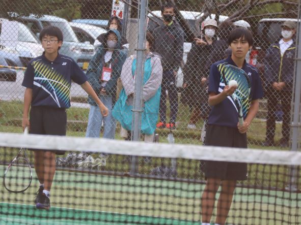 テニスコートで男子生徒たちが試合をしている写真