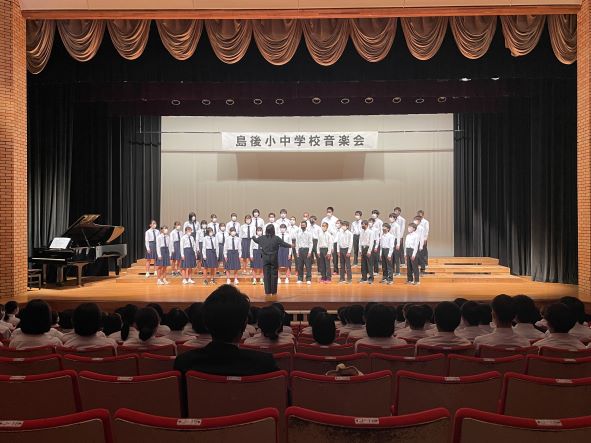 ホールの舞台で生徒たちが合唱をしている写真