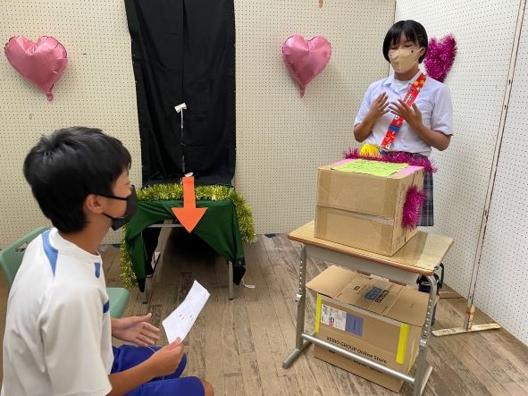 教室でダンボールの前に立つ生徒が出し物をしている写真