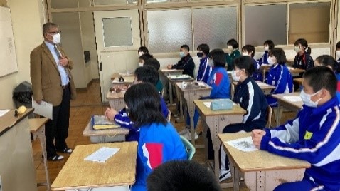 教室でホワイトボードの前に立つ先生が児童たちに授業をしている写真