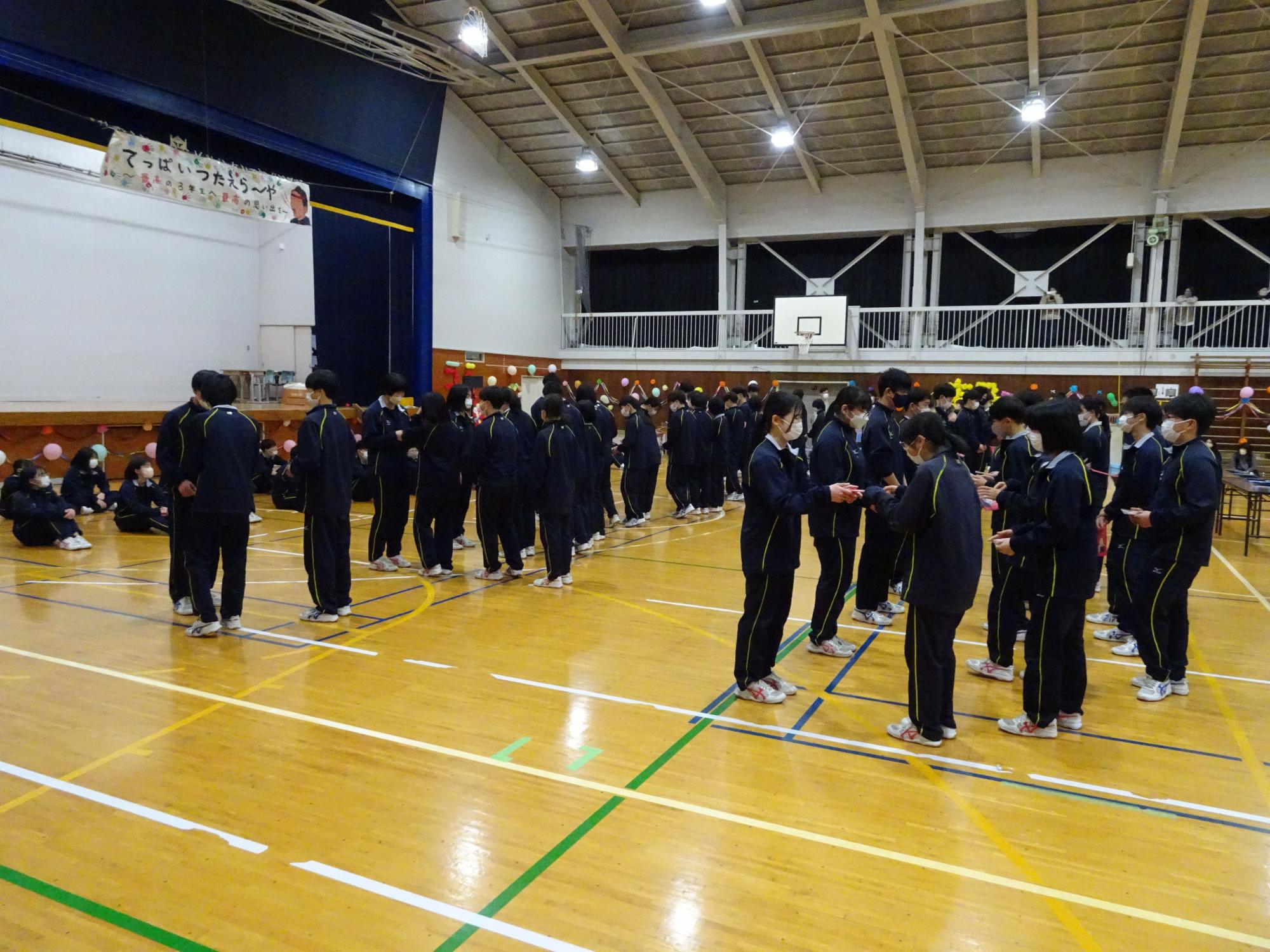 体育館で生徒たちが向かい合って贈り物をしている写真
