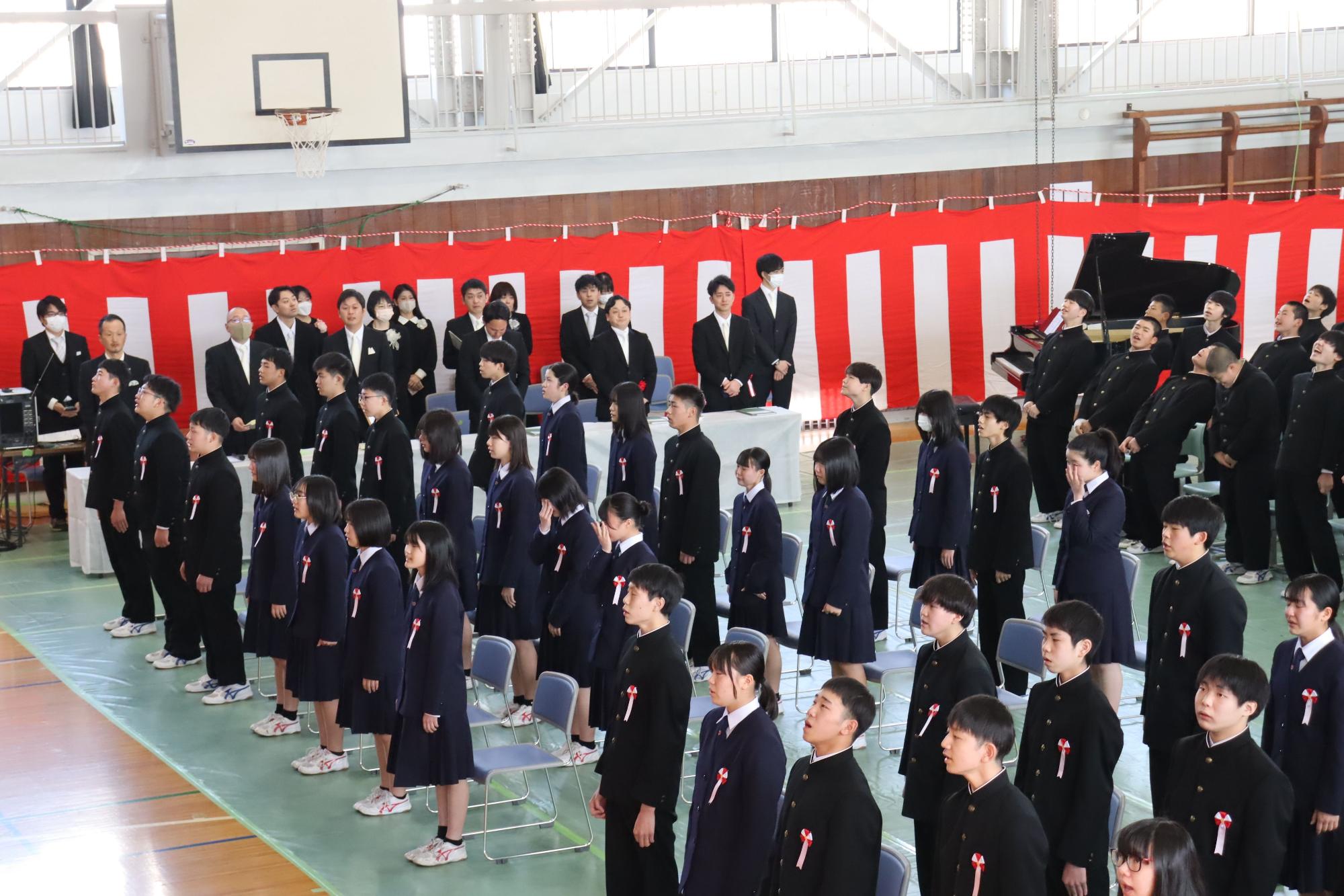 体育館で制服を着た生徒たちが整列し起立している写真