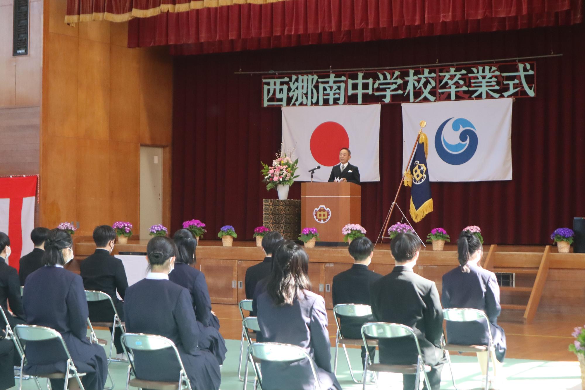 体育館で校長先生が卒業式の式辞を述べている写真