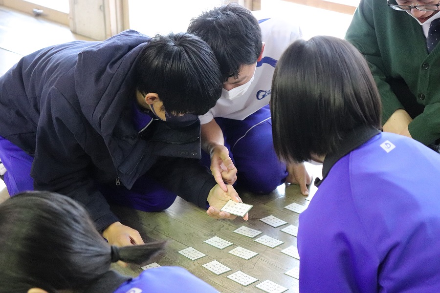 教室で生徒たちが頭を寄せ合ってかるたを楽しんでいる写真