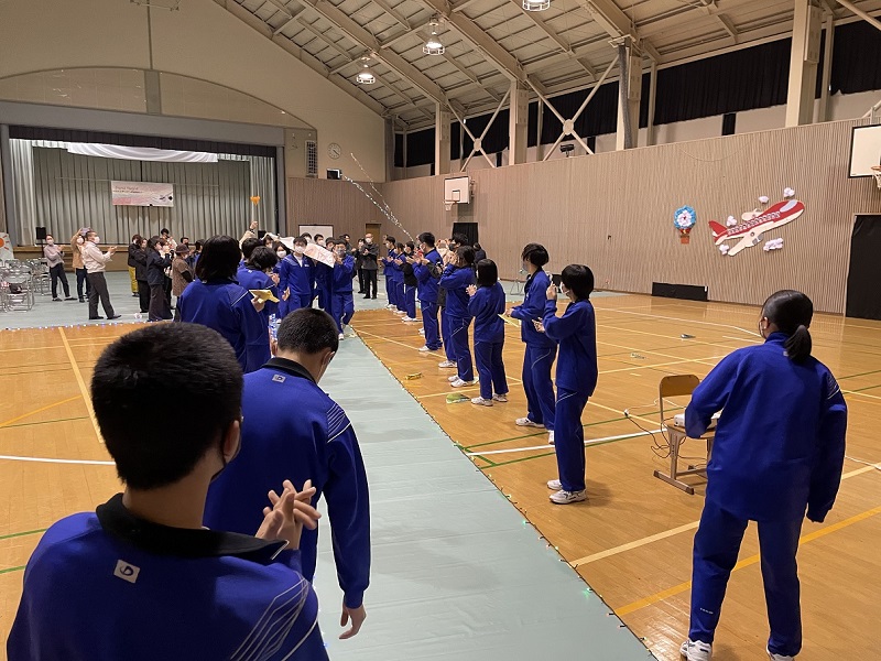 体育館で生徒たちが拍手で見送りをしている写真